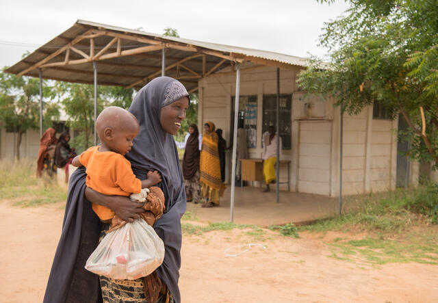 Sukara Hassan Aliyow walks along holding her two-year-old son Mowlid and a bag of nutritious peanut paste.