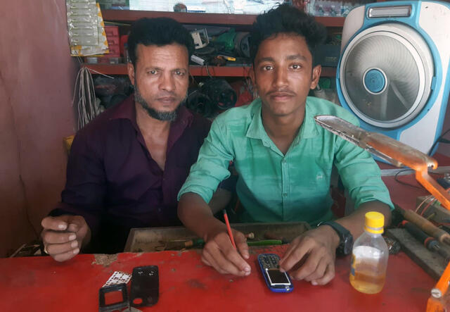 Mujibur (rechts) repariert das Handy von seinem Kunden (links).
