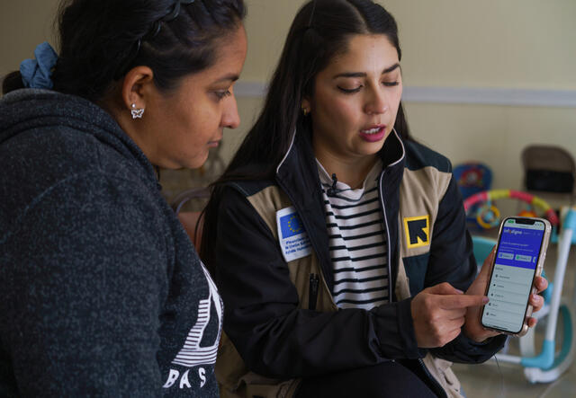 An IRC staff worker stands beside a client, Maria, in Mexico and demonstrates how to access the InfoDigna website on a smartphone.