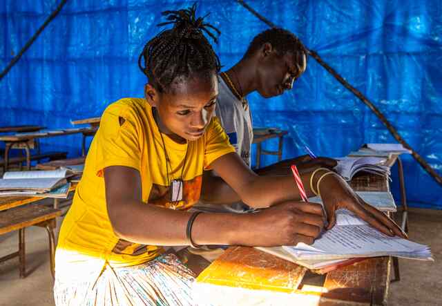 Sixteen-year-old Asamench sits at the front of a classroom where she takes notes. She wears a bright yellow shirt and sits next to a fellow student.