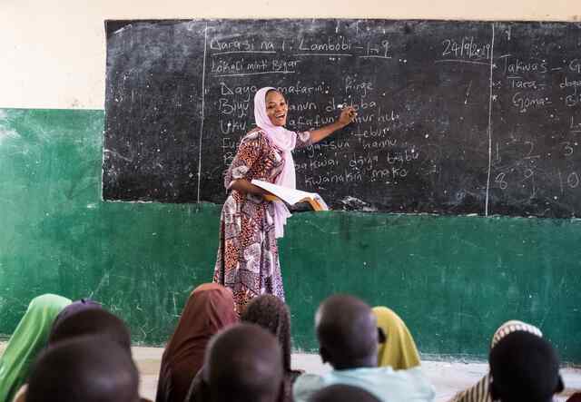 Fatima Musa stands near a blackboard at the front of a classroom in Nigeria where she delivers a seminar to students.