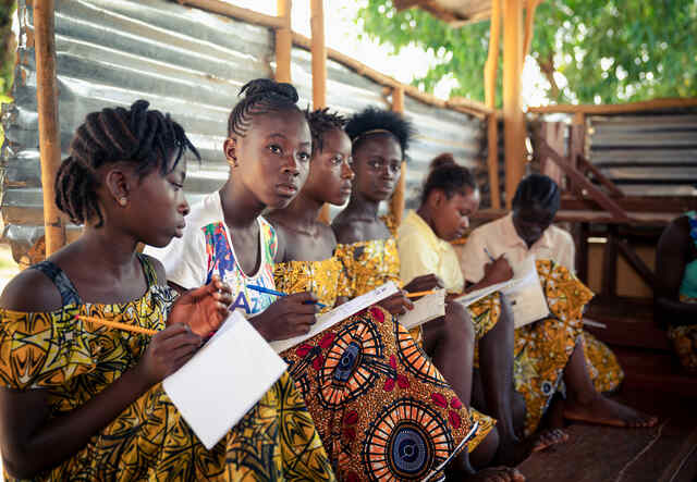 Några tonårstjejer sitter och skriver i sina anteckningsblock under en lektion möjliggjord av EAGER-programmet i Sierra Leone. 
