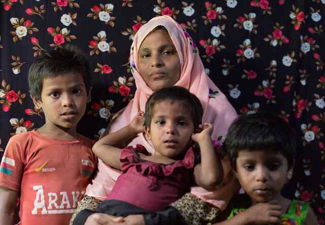 A mother, wearing a pink head scarf, holds one of her young children while two other children stand beside them.