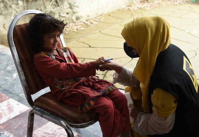 A young girl sits in a chair and smiles while shaking hands with an IRC staff member.