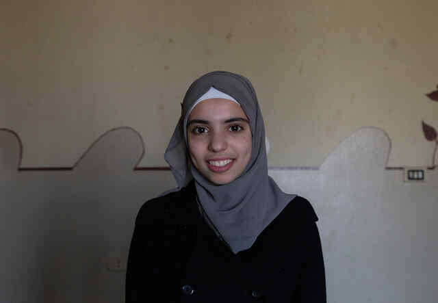 Sabah*, 15, smiles as she poses for a photograph in the living room of their apartment. 