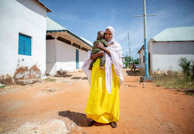 Fartun stands in the street, holding her baby son.