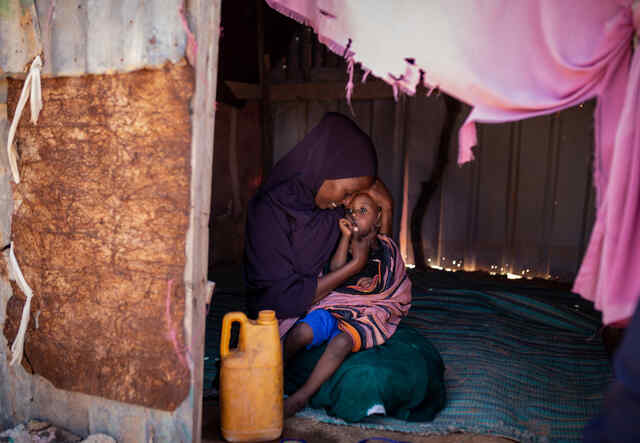 Halima sits, holding her baby in her lap.