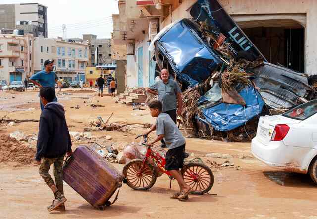 Two boys walk through the affected areas of Derna, Libya. One pushes a bike while the other carries a large suitcase.