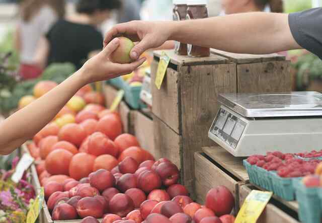 Handla hållbart: två händer möts över ett marknadsstånd med äpplen.