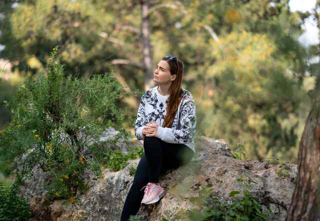 Khystyna sits on a large boulder in the wood and poses for a portrait.