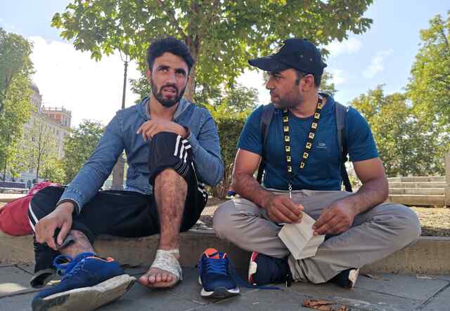 IRC staff sits next to a young man and provides information in front of the Trieste Central Station.