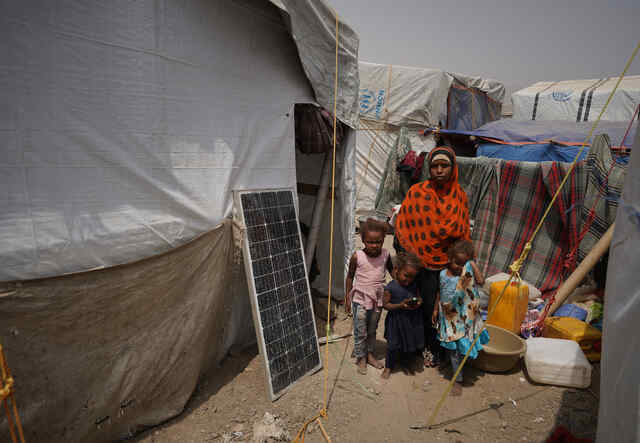 한 여성과 세 명의 아이들이 담요를 뒤로 한 채 텐트 밖 흙 속에 서 있습니다.