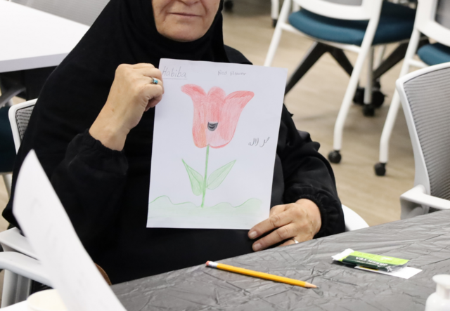 A participant of the Afghan Senior Social Club holding up her drawing of a rose.