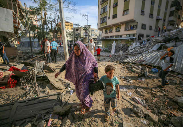 A mother and child walk through the destruction caused by Israeli air strikes in Gaza City.