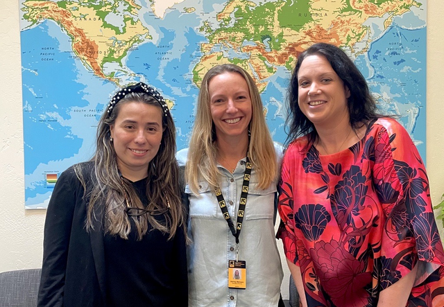 Three women stand together in front of a world map