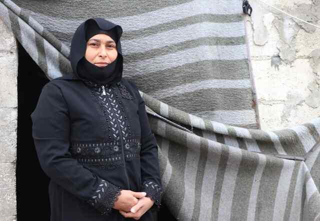 Mustafa, who was displaced from her home Idlib, Syria, poses for a photo outside of a building.