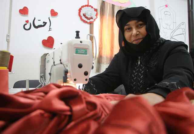 Mustafa sews a red piece of clothing.