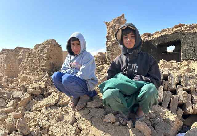 아프가니스탄 소년 두 명이 지진으로 파괴된 건물 잔해 더미 위에 앉아 있습니다.