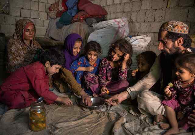 Sajida, ihr Mann und ihre Kinder sitzen in einem Raum auf dem Boden und essen gemeinsam.