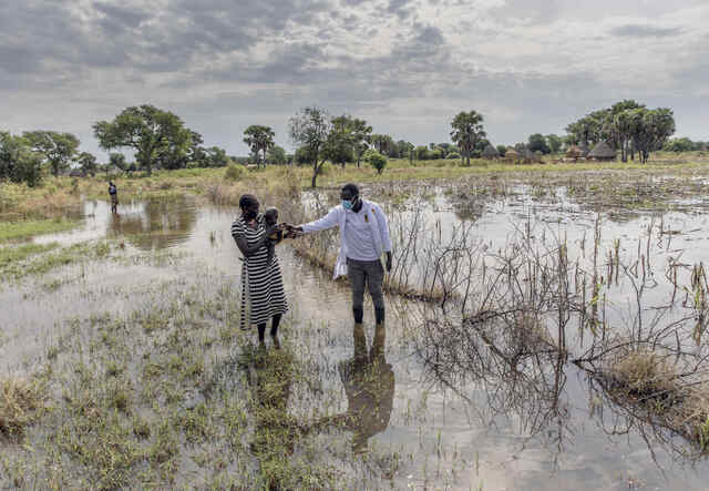 Abuk, holding her 4-year-old son, walks through the floods surrounding her home in South Sudan.