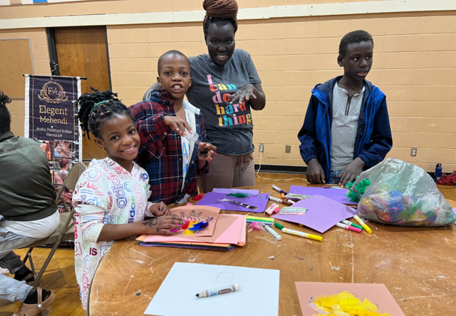 A family of IRC clients, one mother and her three elementary school-aged children, working on arts and crafts and showing off their Henna tattoos