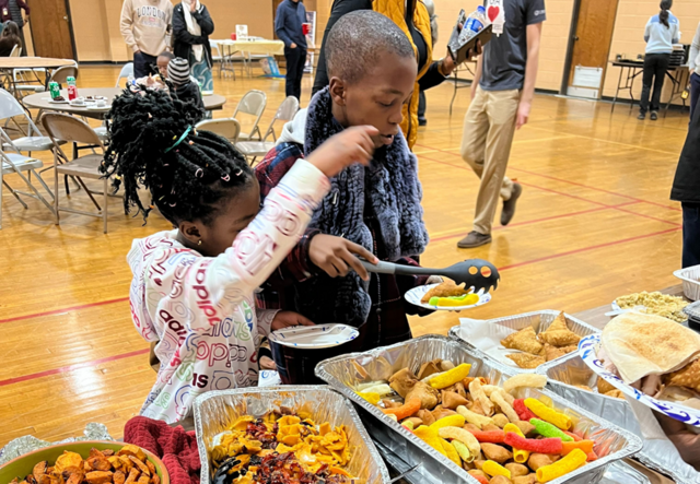 A young girl and boy collecting food from the feast table.