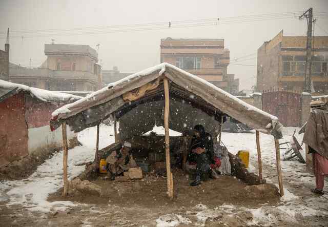 Ein Mann und eine Frau sitzen zusammen in einem kleinen Zelt, das der Witterung ausgesetzt ist, während um sie herum heftiger Schnee fällt.