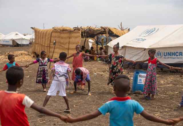 Kinder spielen zusammen im Lager Tunaydbah, Sudan. Die meisten Kinder halten sich an den Händen und bilden einen Kreis um zwei Kinder, die in der Mitte eine Aktivität ausführen.