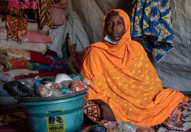 A woman in bright orange sits on the floor of a room. Besides her sits a bowl of assorted foods.