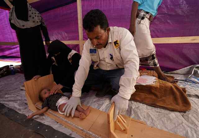 An IRC doctor weighing a baby