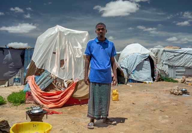 A man stands tall, in front of a number of makeshift shelters in Somalia.