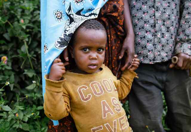 A small child, wearing a yellow shirt, stands in front of an adult.