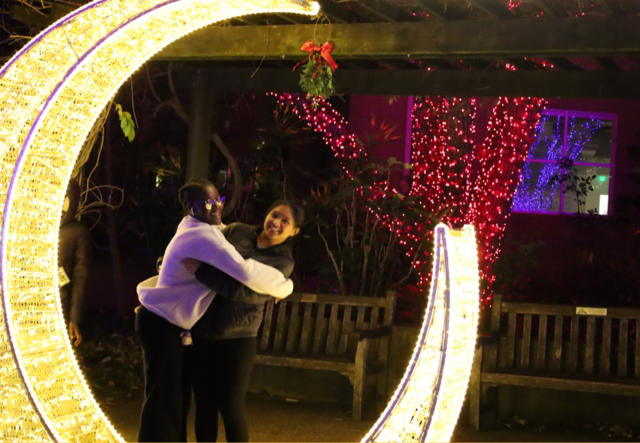 Youth Futures students hugging under the Kiss Me Arch at Garden Lights, Holiday Nights