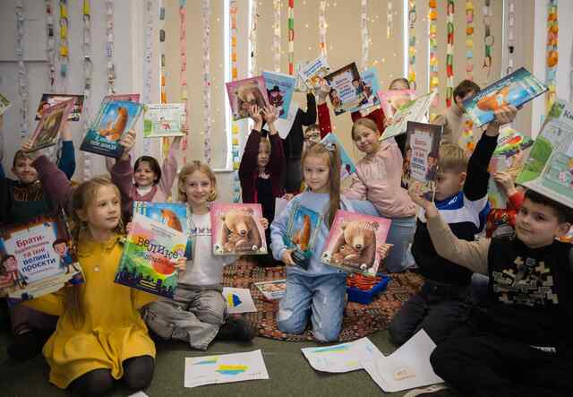 A group of Ukrainian refugee children hold up new books that they've recieved.