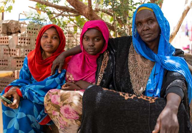 A mother and two daughters stare solemnly into the camera while posing for a portrait.