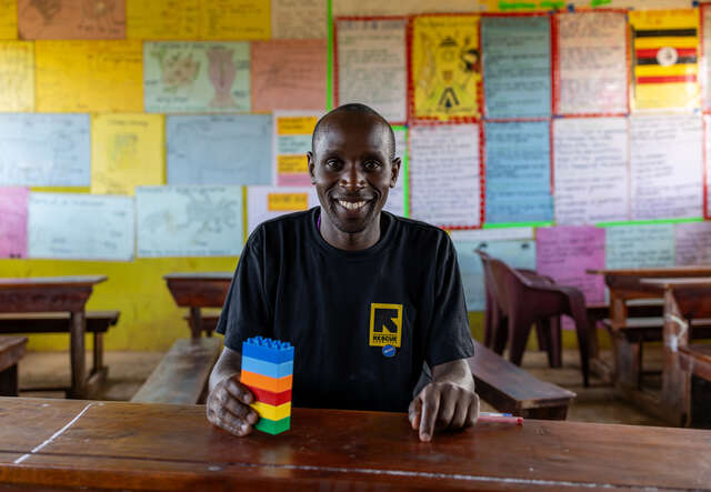 Teacher Izidoro faces the camera smiling and holding a stack of LEGO bricks.