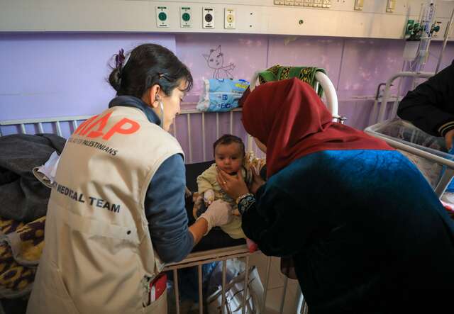 Dr. Jilani tends to a young child at Al Asqa hospital in Gaza next to another hospital staff member.