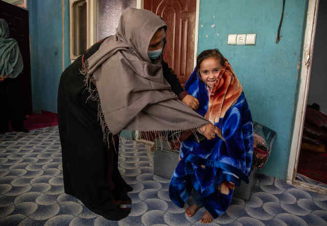 아프가니스탄 카불에 있는 그들의 집 밖에서, 한 엄마가 웃고 있는 딸을 새로산 담요로 감싸고 있습니다.