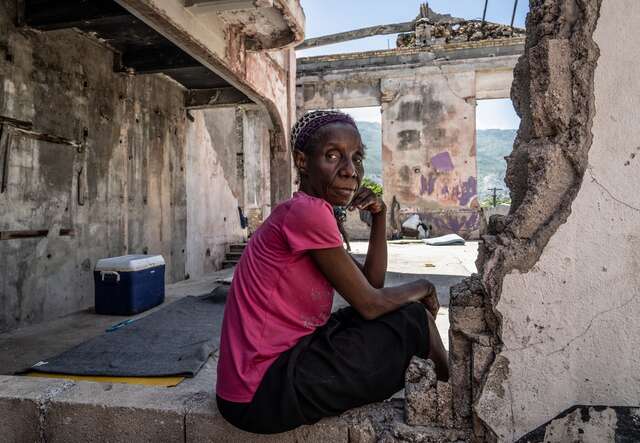 A middle-aged woman leans down and poses for a picture in a ruined building in Port-au-Prince, Haiti.