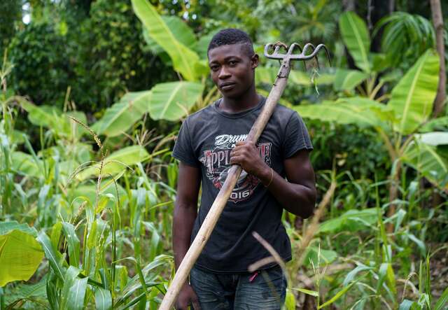 A man stands in a field, holding garden tool.