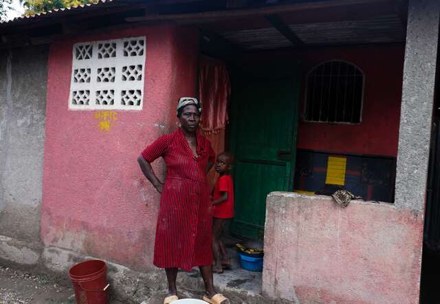 A woman and a child pose for a picture, standing together just outside a red house in Haiti.