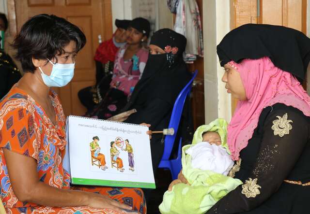 An IRC health promoter points to a sign and delivers messages on infant care to a new mother.