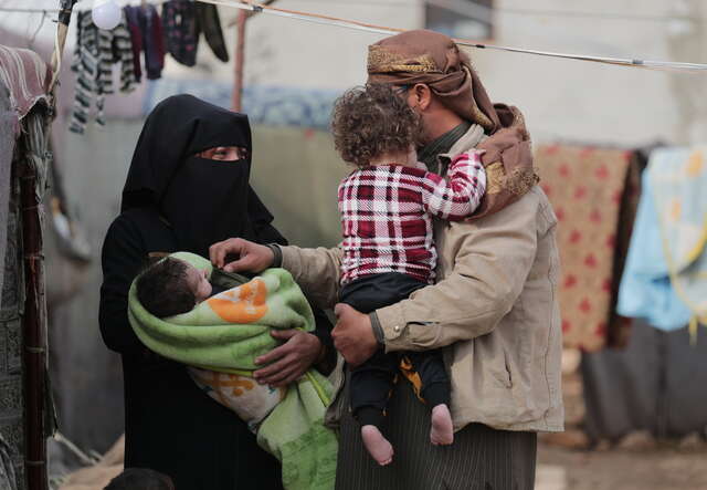 En familj på fyra står tillsammans vid tältet som de bott i sedan jordbävningen i Syrien och Turkiet. 