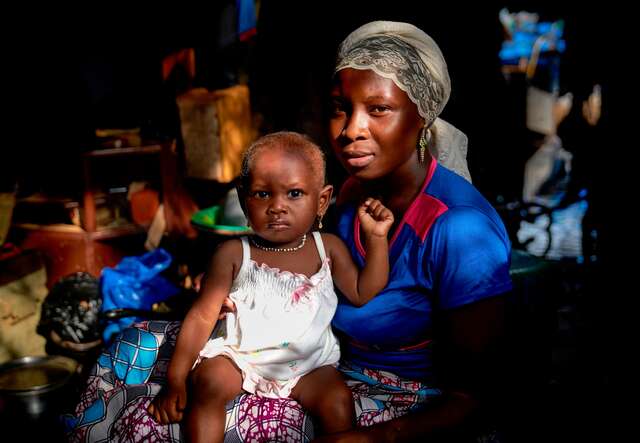 A portrait of a Malian mother holding her child in their home.