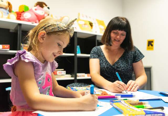 A young girl completes a learning activity at an IRC Safe Learning and Healing Space alongside her mother in Poland.