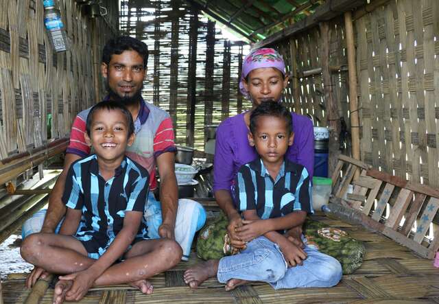A father and mother pose for a family portrait with their two sons in their home in Myanmar.