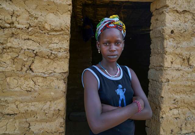 A girl poses for a portrait, staring solemnly into the camera with her arms crossed.