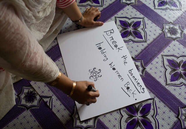 En kvinna skriver på ett plakat "Break the barriers holding women down."