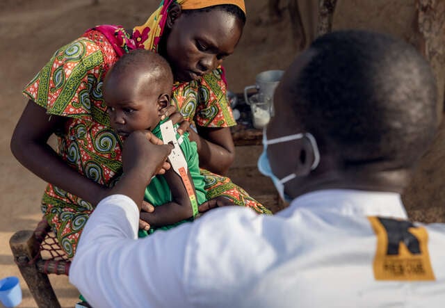 En mamma i Sydsudan håller sin son i knäet medan RESCUE:s medarbetare visar hur mätbandet för undernäring används.