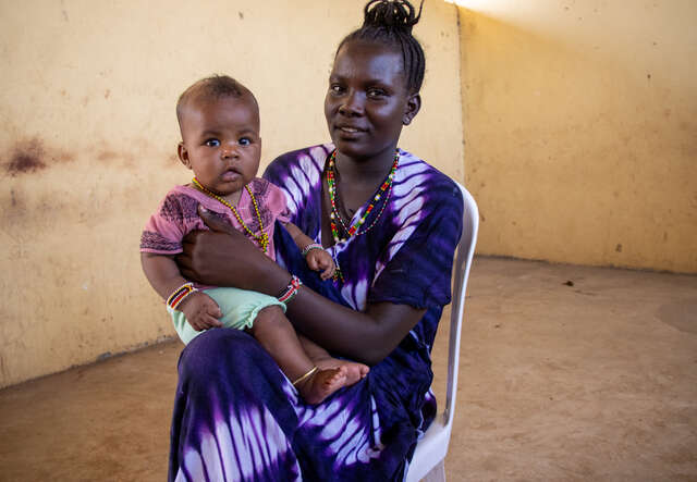 A mother sits in a chair and poses for a photo while holding her young daughter.